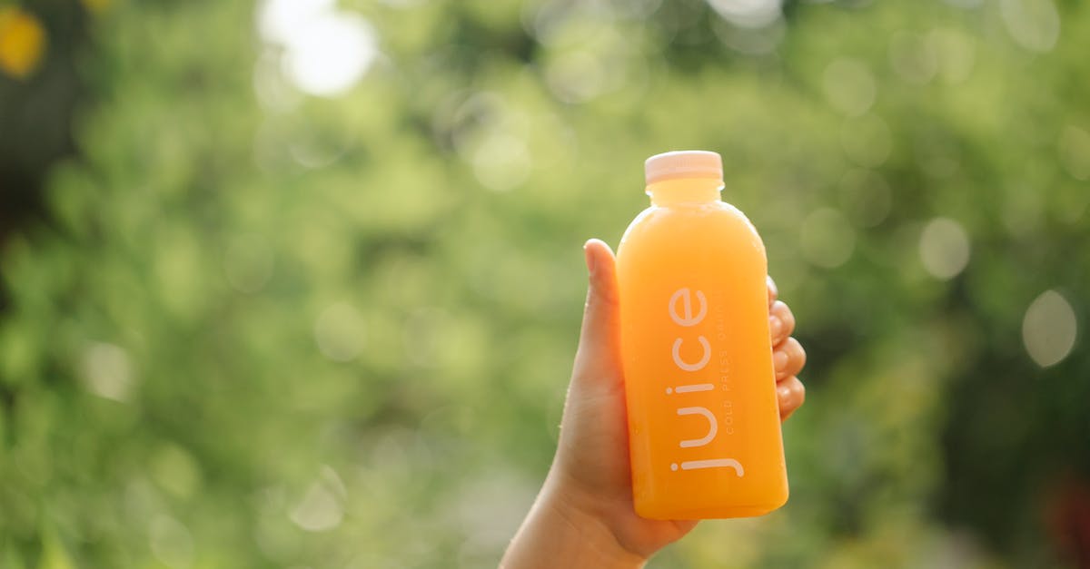 1.9 tellraw selector color showing as green - Unrecognizable person demonstrating bottle of orange juice while standing in nature with green trees and lush foliage on blurred background