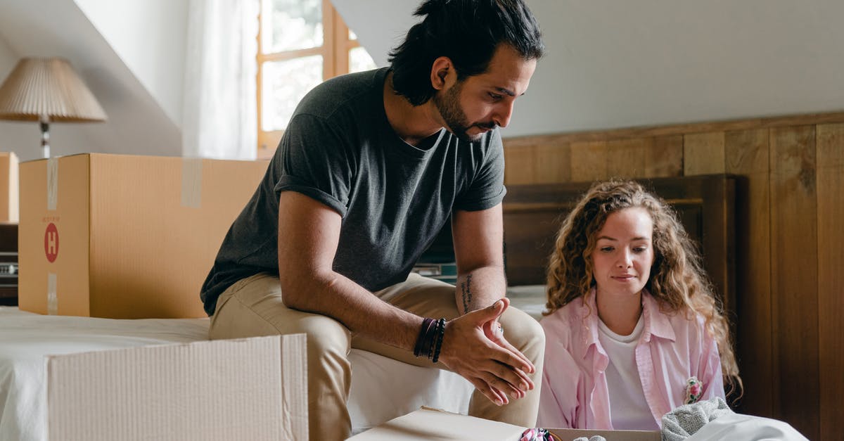 A Nickel that can't be picked up - Content adult ethnic man and woman in casual clothes sitting together in attic bedroom of new apartment among cardboard packages while unpacking stuff