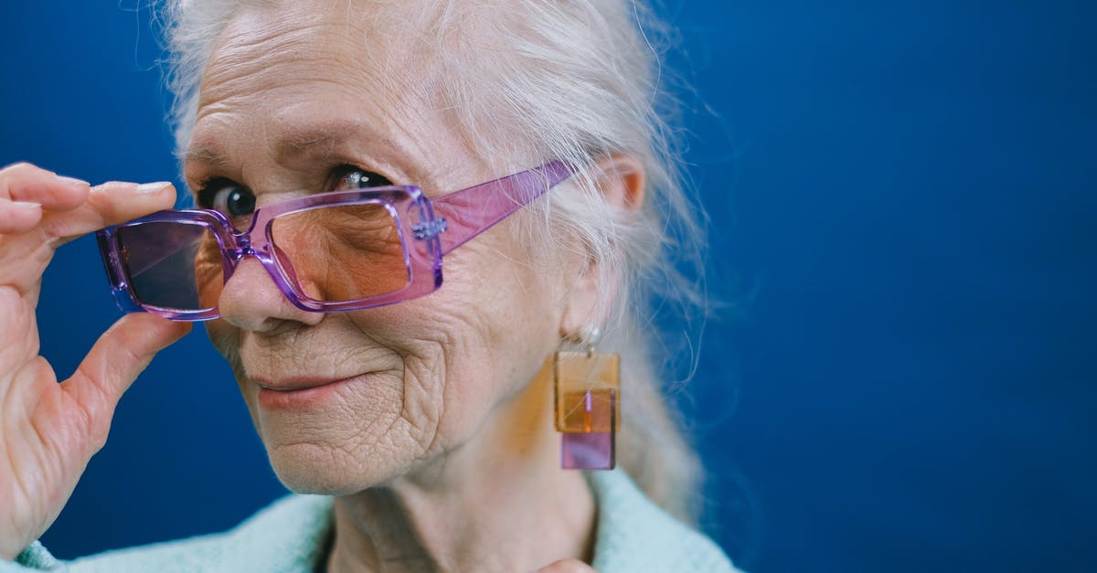 Accessibility in Age of Empires II - Portrait of elegant smiling gray haired elderly female wearing purple sunglasses and earrings looking at camera against blue background