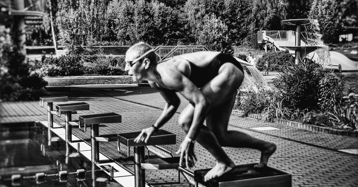 Activate clock only when command block output is true - Black and white side view full body sporty swimmer in swimming suit and goggles standing on block in track start position preparing to dive in outside pool Activate clock only when command block output is true - Black and white side view full body sporty swimmer in swimming suit and goggles standing on block in track start position preparing to dive in outside pool