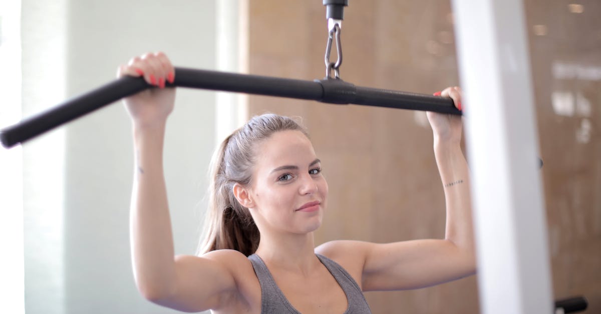 Adding multiple pokemons to a friendly gym without training after taking over a gym - Young friendly muscular woman in sports bra doing exercises using training apparatus and looking at camera during arm training in fitness center