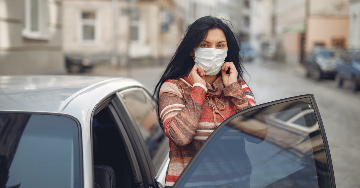 Adjust latency in multiplayer mode to solve car input lag - Young woman wearing medical mask standing near automobile on empty urban street