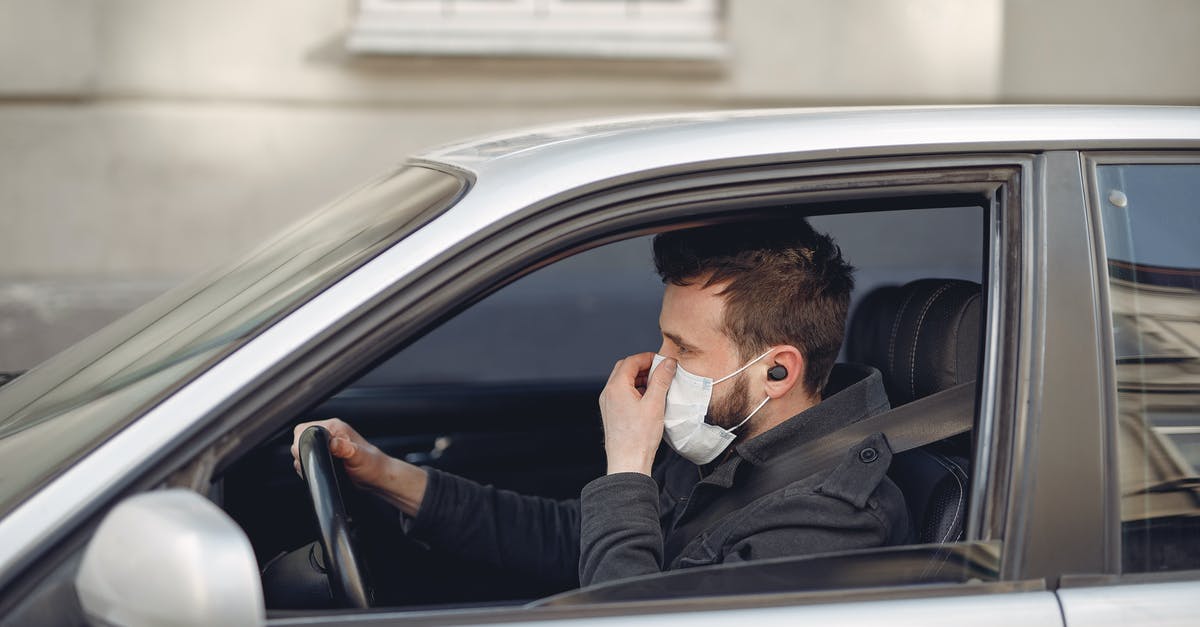 Adjust latency in multiplayer mode to solve car input lag - Serious man in disposable mask and earbuds driving car at daytime