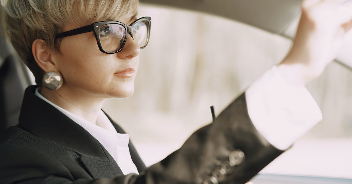 Adjust latency in multiplayer mode to solve car input lag - Side view of crop female driver in stylish formal outfit and eyeglasses with takeaway coffee looking at rear mirror of modern car