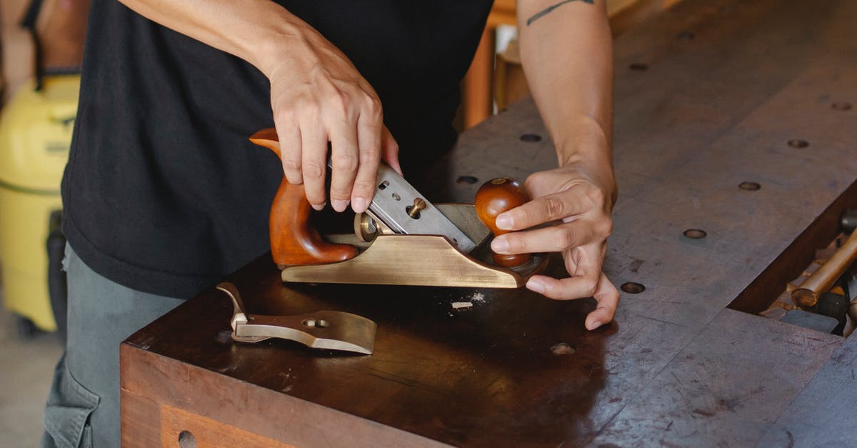 Adjust third person view when inside a workshop area - Anonymous male carpenter with tattoo adjusting knife in planer for cutting wood during work in professional workshop on blurred background Adjust third person view when inside a workshop area - Anonymous male carpenter with tattoo adjusting knife in planer for cutting wood during work in professional workshop on blurred background