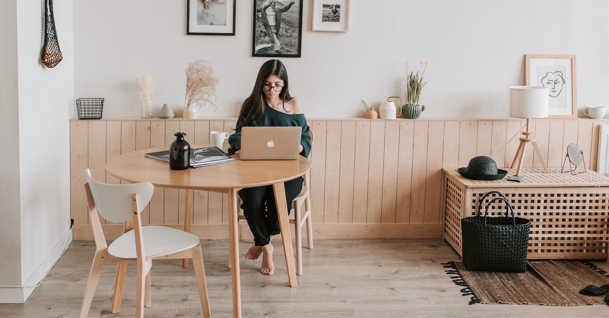 Advantage of using Low Grade Fuel compared to Wood - Full length of pensive brunette in eyeglasses sitting at table with legs crossed and working on laptop in cozy creative living room