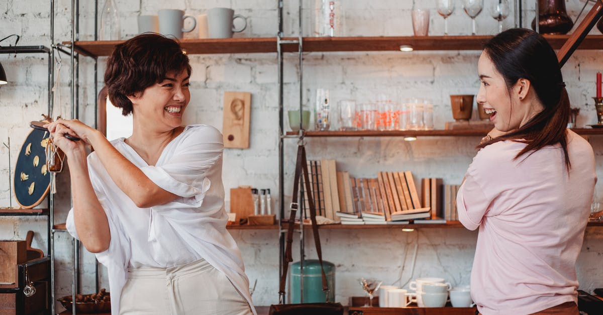 Android Play store additional content download location? - Young ethnic female buyers interacting while laughing near shelves with kitchen items and looking at each other in store