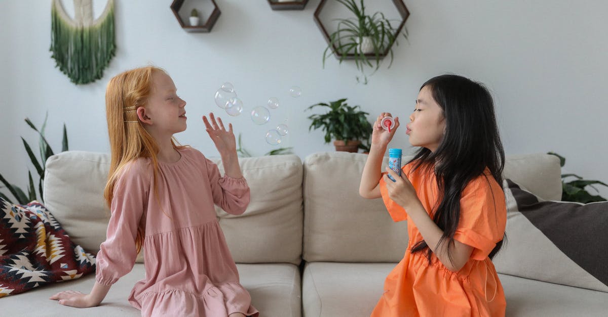 Are the live games casted in real time or is there a 2 min delay? [closed] - Side view of cheerful little diverse girlfriends in trendy dresses sitting on comfortable sofa in cozy living room and blowing soap bubbles