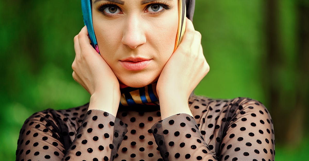 Are there any advantages to having an axe with silk touch? - Crop serious female wearing silk headscarf holding face in hands and looking at camera attentively while standing in lush garden