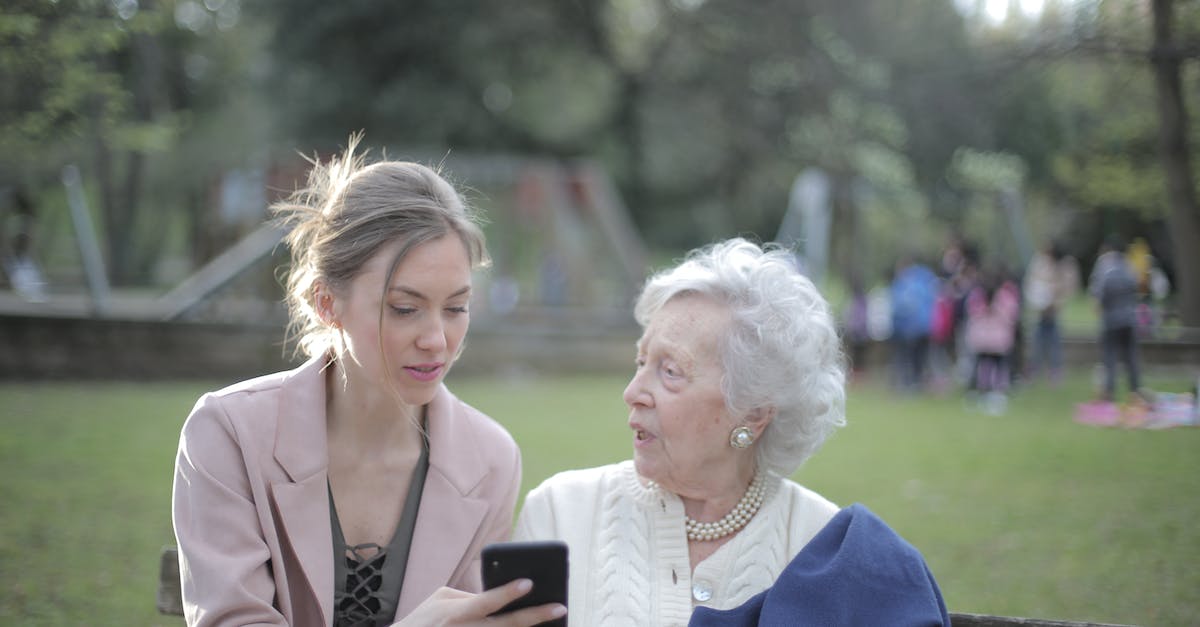 Auto-attack behavior relative to ability use - Adult daughter teaching senior mother using smartphone in park Auto-attack behavior relative to ability use - Adult daughter teaching senior mother using smartphone in park