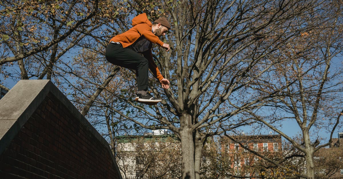 Autumn season challenge - Energetic man jumping from brick wall in city park Autumn season challenge - Energetic man jumping from brick wall in city park