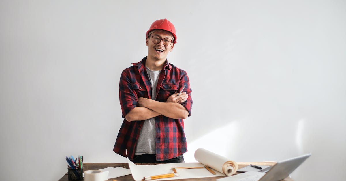 Basic attack strategy for Civilization 5 - Smiling casual man in hardhat and glasses holding arms crossed looking at camera while standing at desk with paper draft and stationery