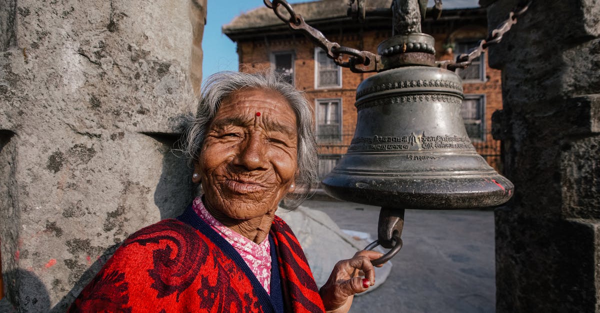 Bell puzzle in the Temple of Eothas - Cheerful elderly Hindu female in bright apparel touching aged temple campane and looking at camera on street