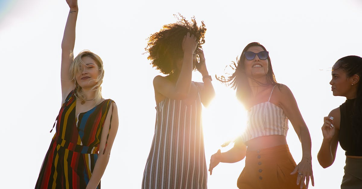 Best move when they are no more certain moves left - From below of young content diverse ladies in trendy outfits smiling and dancing against cloudless sky during open air party on sunny day