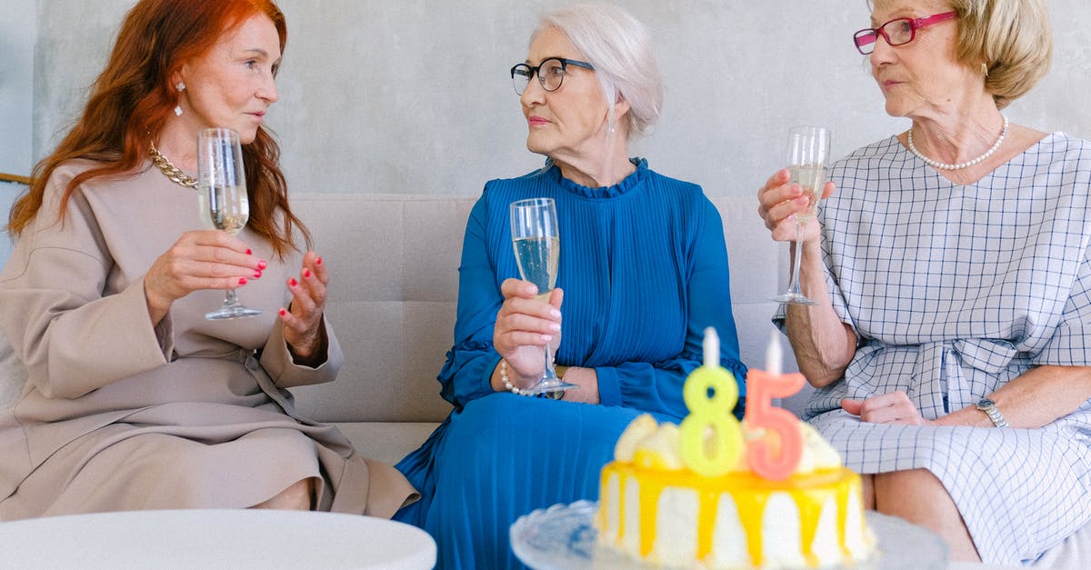 Best way to utilize cake - Aged best friends with glasses of champagne talking at table with birthday cake decorated with candles