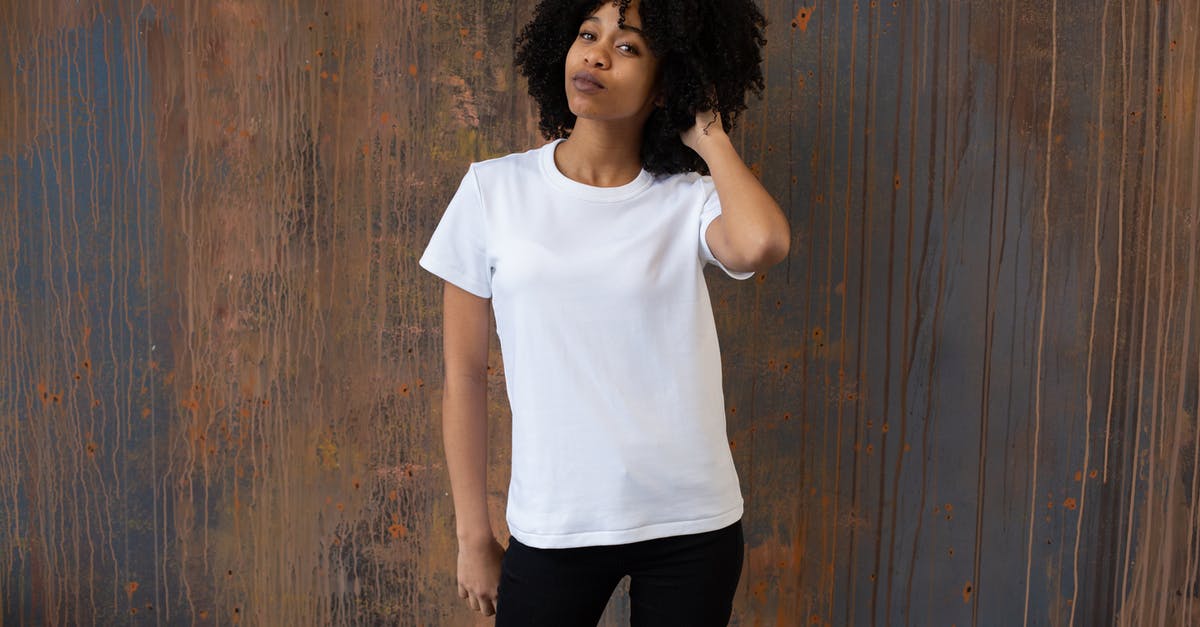 Bloodskal Barrow won't appear - Self assured young African American lady in casual outfit touching dark curly hair and looking at camera while standing against wooden wall in studio