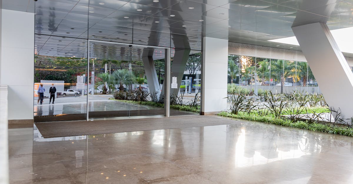 Building academy on oil tile - Auto acquire oil? - Concrete columns of modern office building with reflective glass doors at entry under tiled ceiling Building academy on oil tile - Auto acquire oil? - Concrete columns of modern office building with reflective glass doors at entry under tiled ceiling