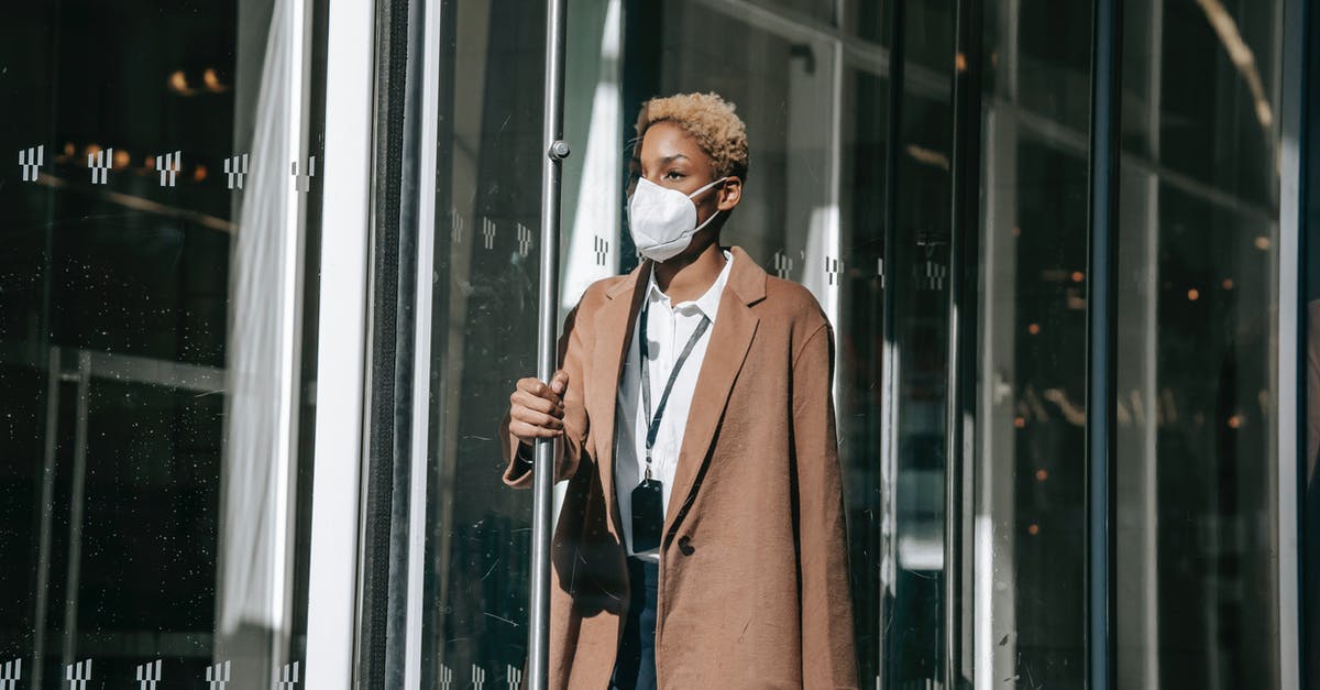 Building normally open floodgates - Serious young black lady in mask opening modern building door after workday Building normally open floodgates - Serious young black lady in mask opening modern building door after workday