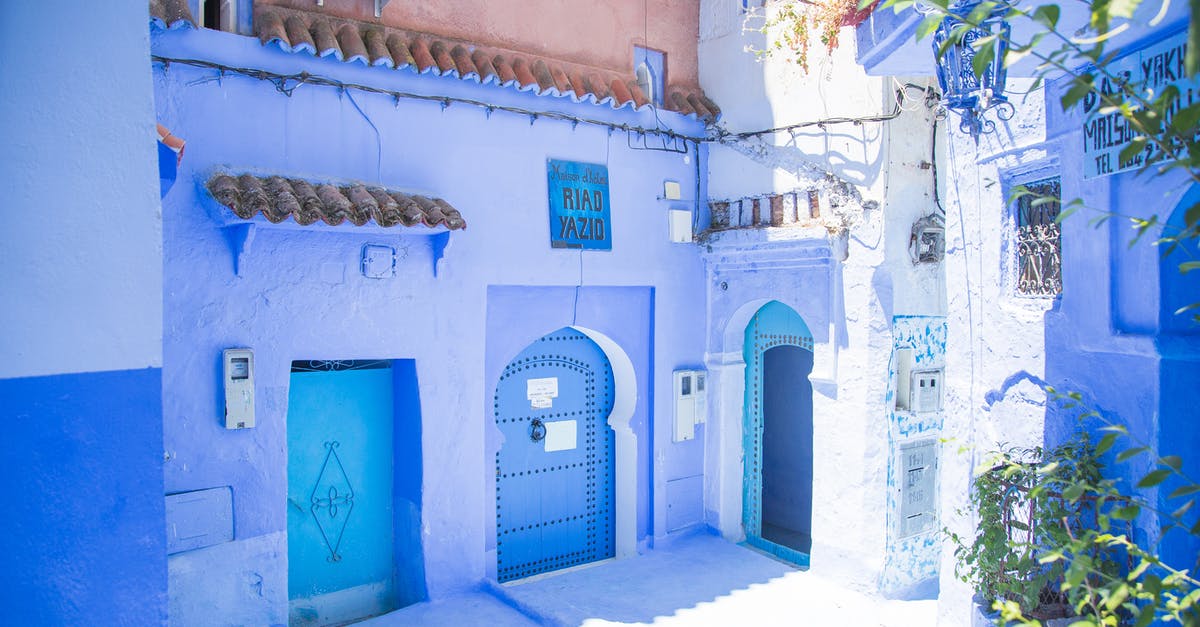 Building utilities on a wall corner - Blue exterior of house with doors located under sunlight on street with green plants in city of Morocco in summer