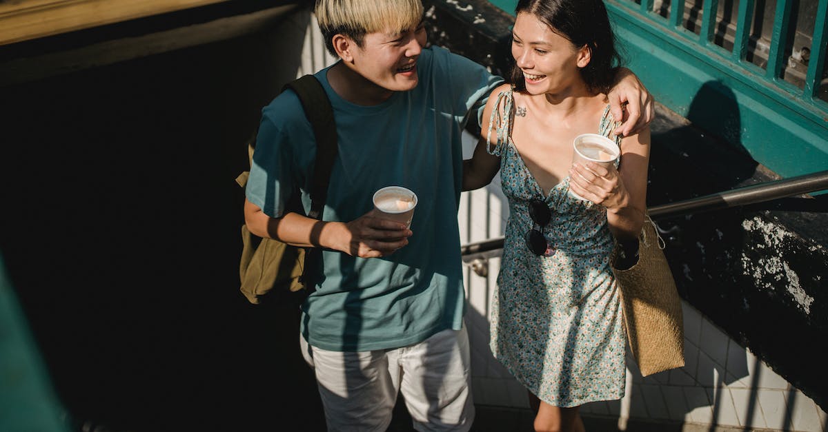 Bye bye love - Where do I go from here? - From above of cheerful Asian couple with coffee looking at each other and hugging while getting out of subway station Bye bye love - Where do I go from here? - From above of cheerful Asian couple with coffee looking at each other and hugging while getting out of subway station