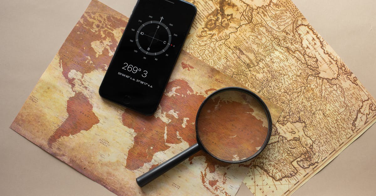 Can't Find Llamas! - Top view of magnifying glass and cellphone with compass with coordinates placed on paper maps on beige background in light room