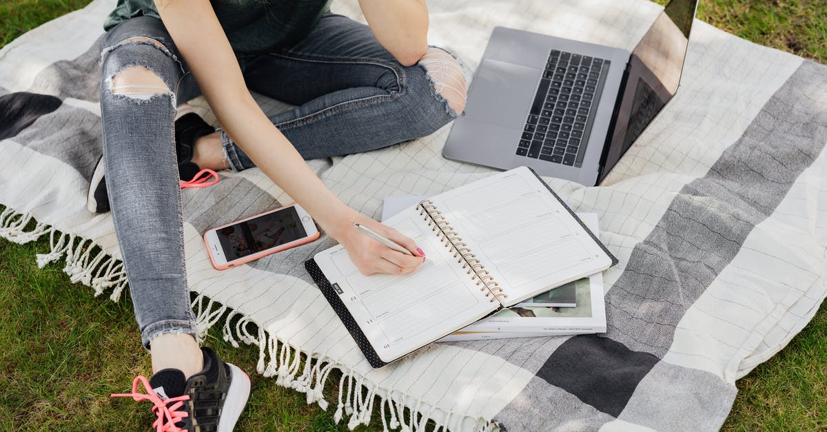 Can't learn Master Smithing from Eorlund Graymane? - From above crop anonymous female student in casual outfit writing in planner while sitting on warm blanket with smartphone and laptop on green park lawn