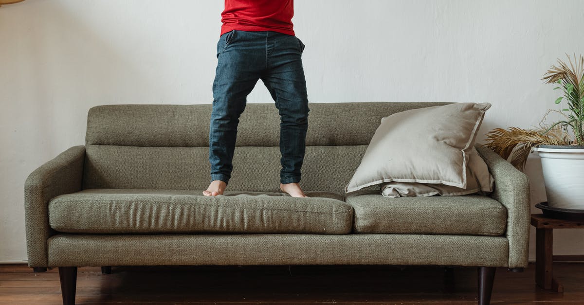 Can't play minecraft - Unrecognizable barefoot boy in casual clothes jumping on sofa while spending time in cozy living room with modern interior