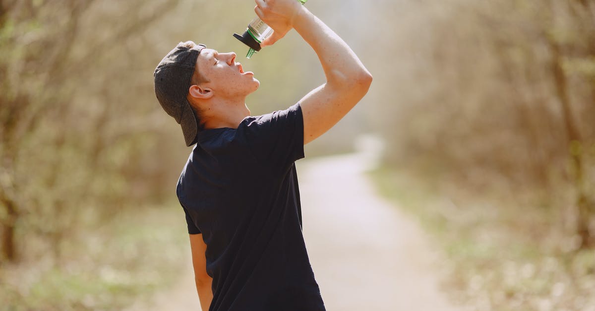 Can't run any program in - Side view of young male athlete wearing sports clothes and cap drinking water from plastic bottle on blurred background of forest during running and workout Can't run any program in - Side view of young male athlete wearing sports clothes and cap drinking water from plastic bottle on blurred background of forest during running and workout