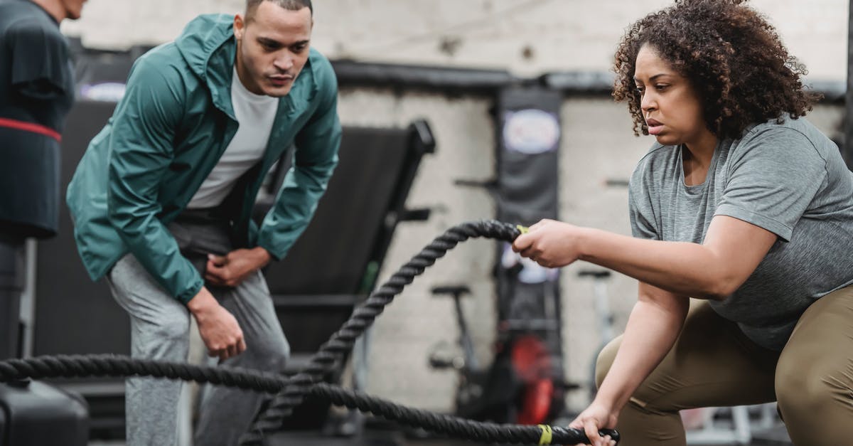 Can a gym get free without battling? - Plus sized African American female in sportswear exercising with battle ropes near serious male instructor during intense workout in modern fitness center Can a gym get free without battling? - Plus sized African American female in sportswear exercising with battle ropes near serious male instructor during intense workout in modern fitness center