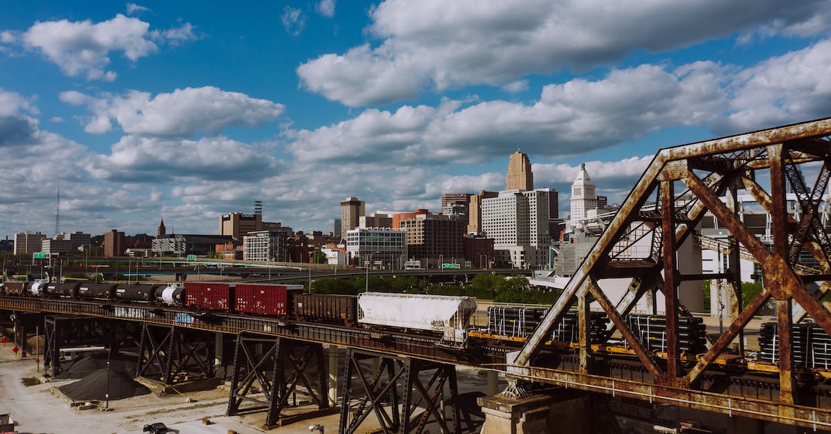 Can a train cross this junction? - Freight train crossing railway bridge near industrial buildings against blue sky with clouds on sunny summer day