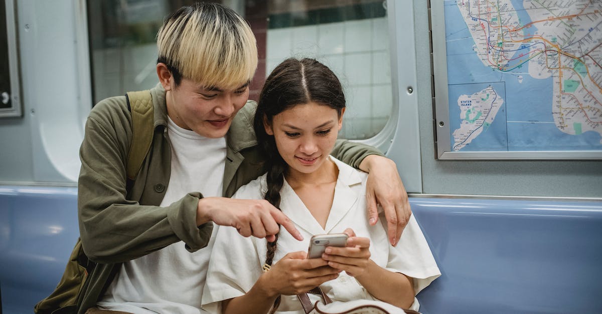 Can cargo trains and passenger trains share the same line? - Happy young trendy Asian guy hugging smiling girlfriend and pointing at smartphone screen while commuting by subway train