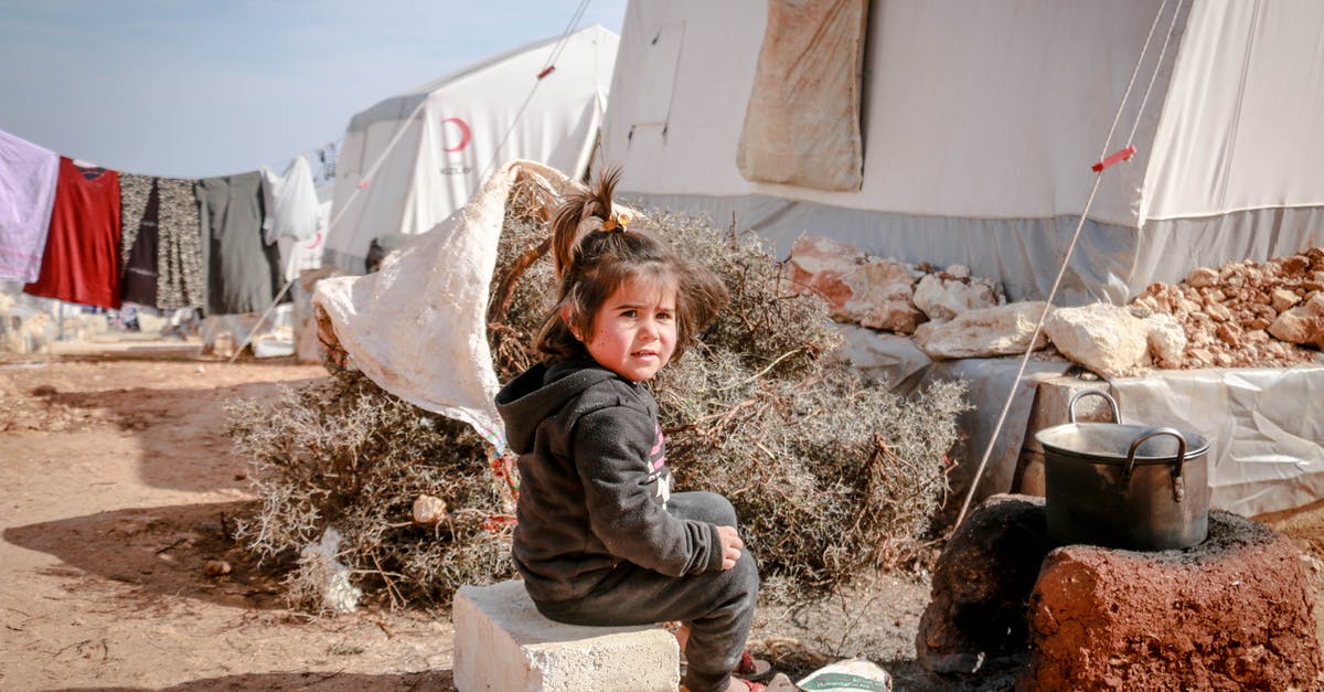 Can destroy command to destroy a certain type of block - Full body ethnic girl looking at camera over shoulder while sitting on concrete block near hearth outside tent in refugee camp