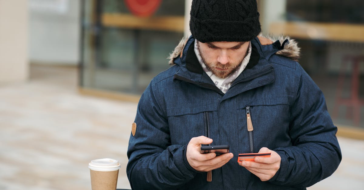 Can GTA Online money be transferred to single player? - Focused male holding credit card while making payment with smartphone on street