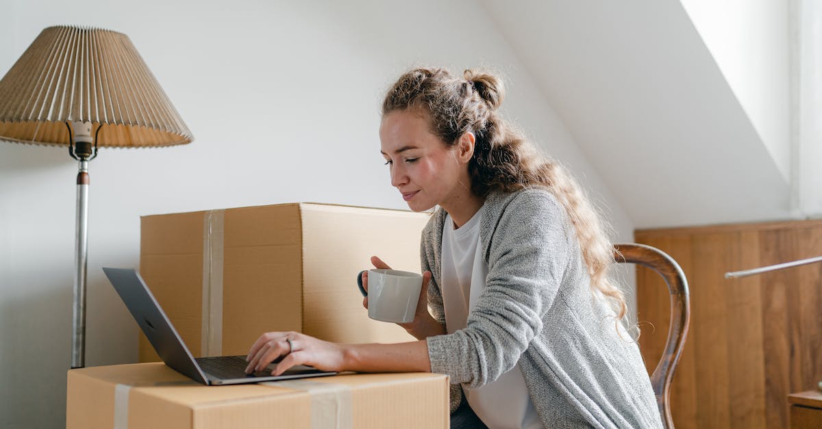 Can I break a box or otherwise extract contents without touching? - Content lady in casual wear typing on netbook while sitting on chair with cup of hot drink near big cardboard boxes in light apartment