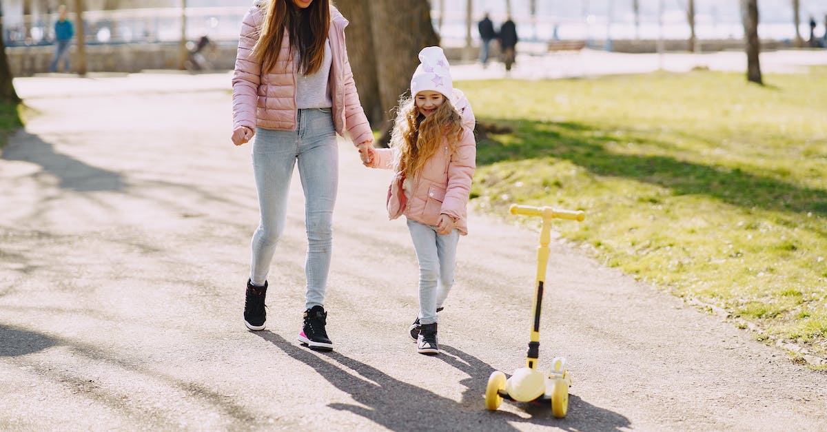 Can I buy season 2 of The Walking Dead one game episode at a time? - Full length female and little girl in warm clothes holding hands while walking and playing on walkway in city park near trees in sunny day