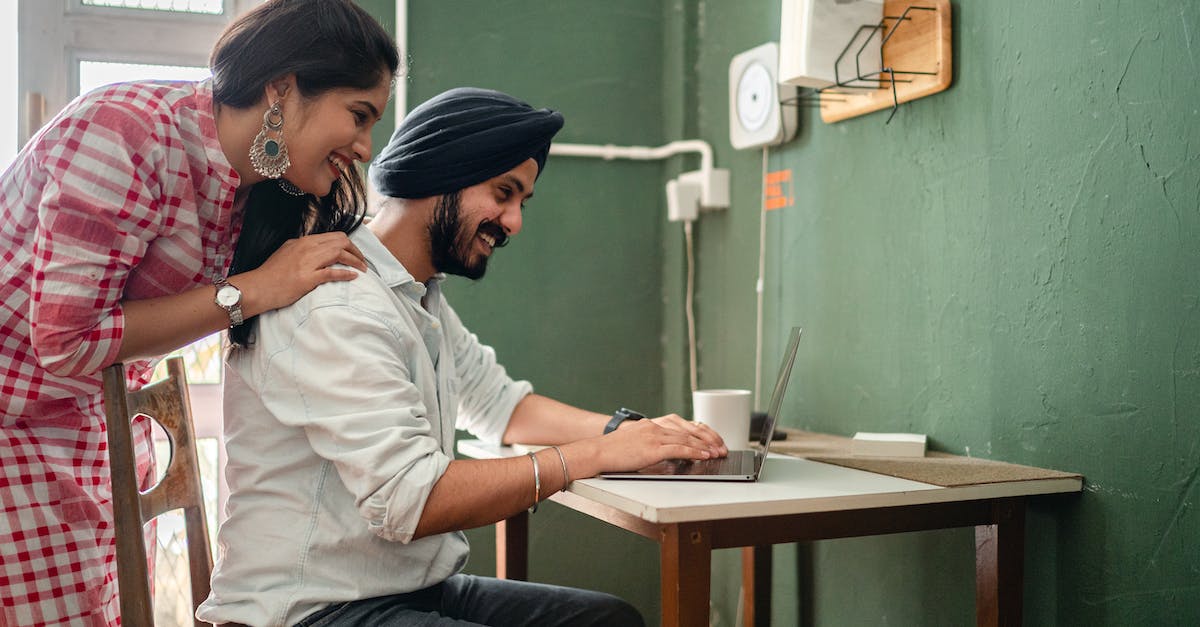 Can I copy "not-on-PSN" games from PC back to my Vita? - Side view of cheerful adult couple in casual outfit using netbook at table in kitchen while woman bending over man touching back