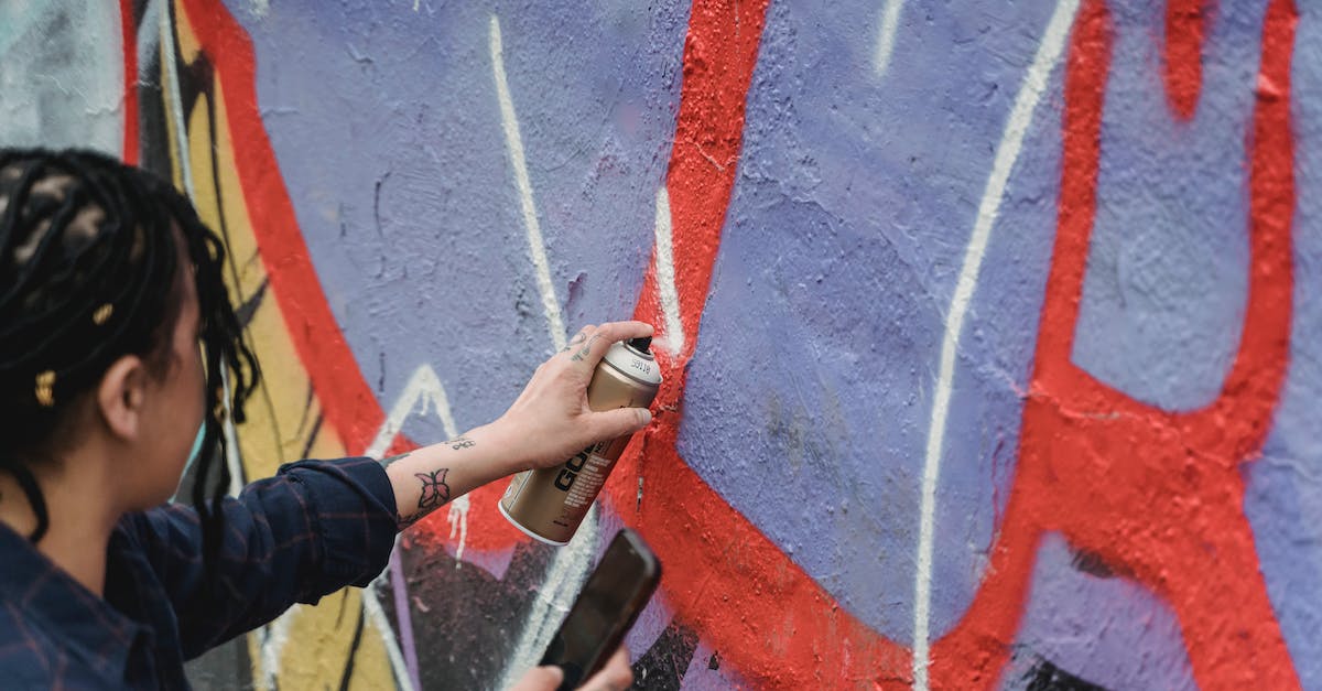 Can I extract skills from my weapons? - From above side view of crop faceless female artist with braided hair painting graffiti on wall while standing on street