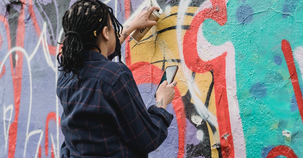 Can I go back and change my reward from the Color Dungeon? - Back view of unrecognizable female artist with black braided hair painting graffiti on wall with spray paint can on street