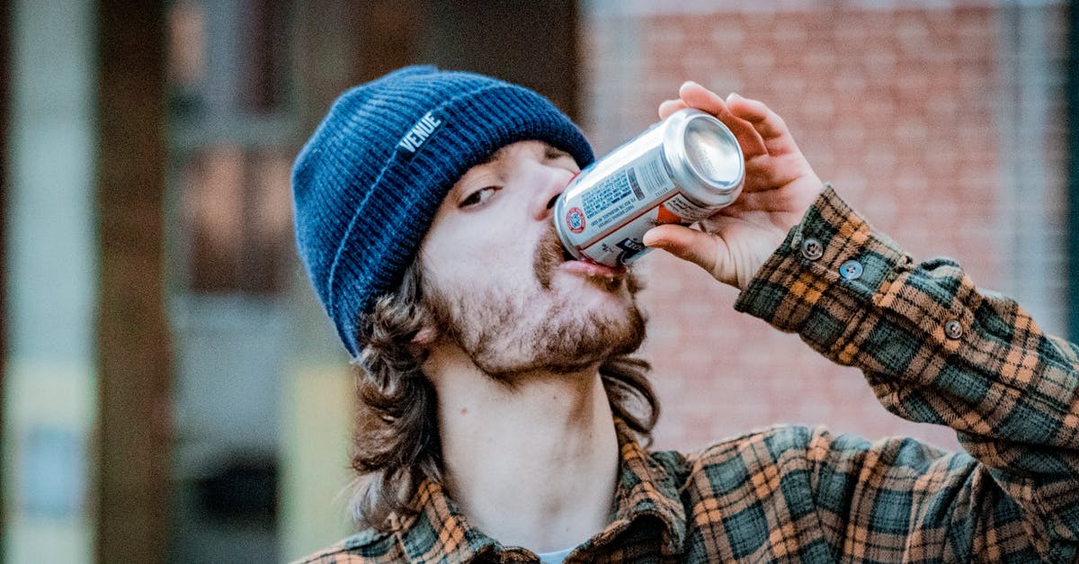 Can I hold more than 10 healing items? - Calm young male in casual checkered shirt and hat enjoying cold drink from can while standing on street and looking at camera