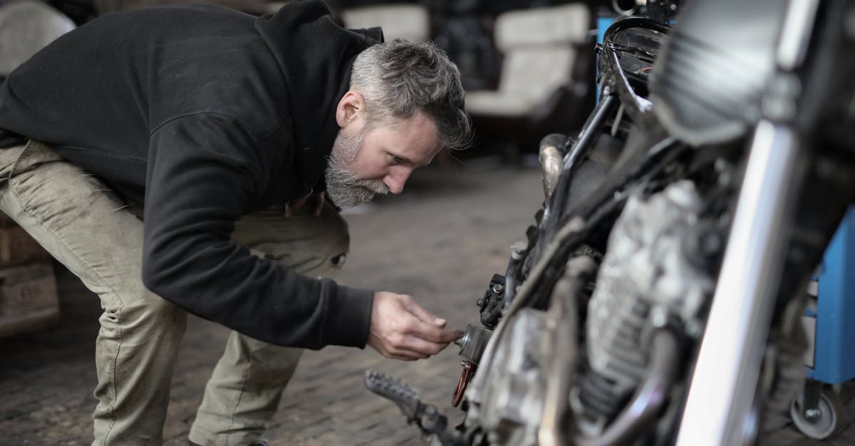 Can I repair my helicopter ? - Side view of serious male master in untidy casual clothes standing near motorbike and checking details while working in garage