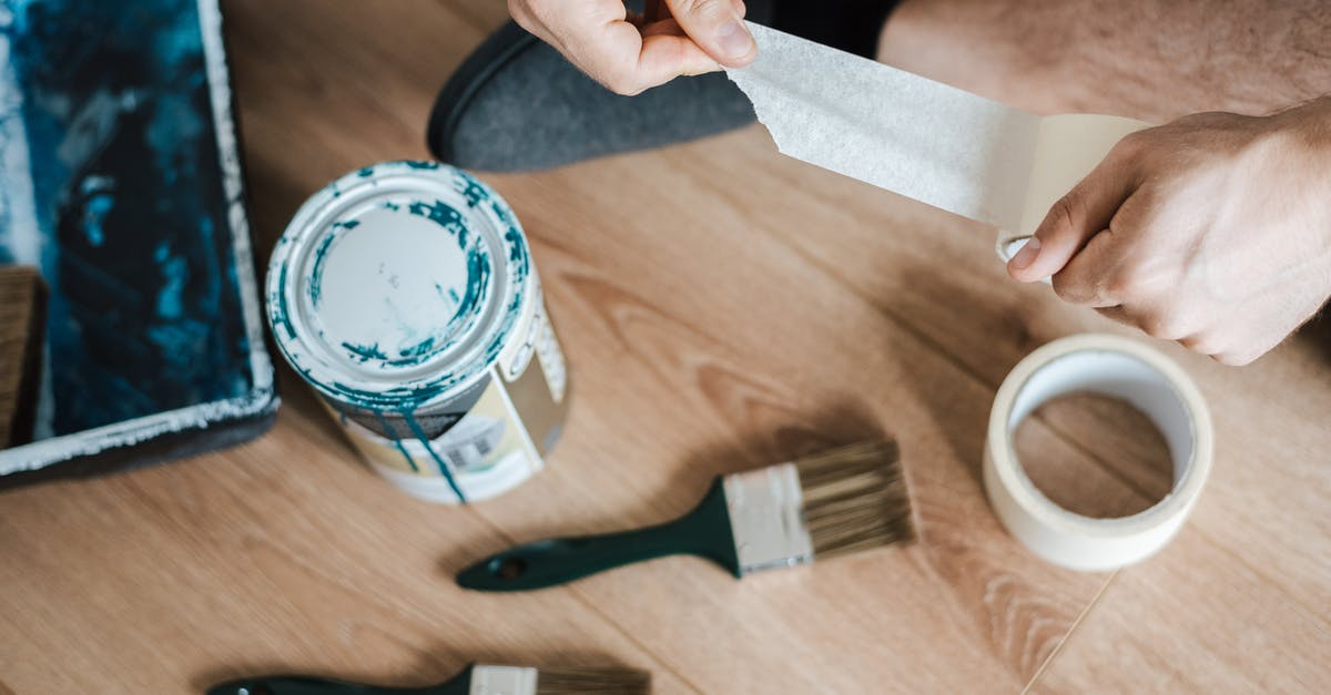 Can I safely steal from shops while invisible? - From above of crop anonymous male unwrapping sticky tape roll on parquet near paint brushes in house