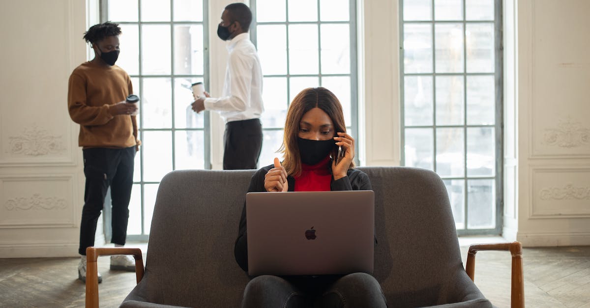 Can I talk to people without digging up their past? - Ethnic female worker in fabric mask with netbook and thumb up speaking on cellphone against male partners with takeaway coffee