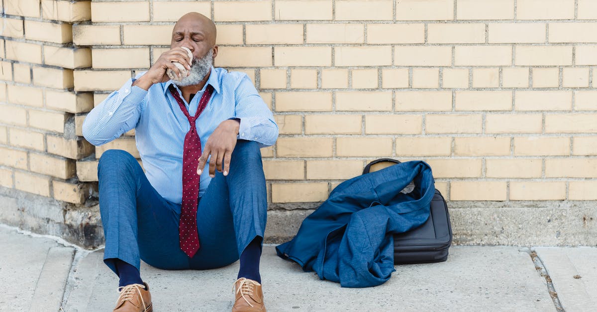 Can I upload full playthroughs onto YouTube? - Full body of mature African American bearded businessman in blue trousers and light shirt with maroon tie sitting on ground at brick wall and drinking beverage from tin can