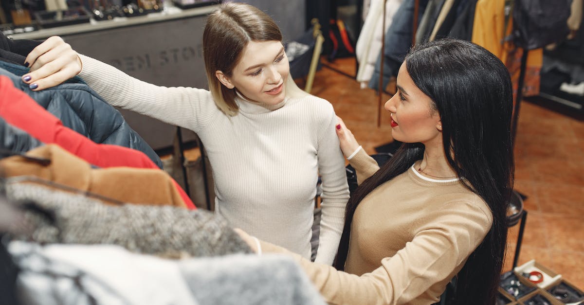 Can I view tags from other languages without switching my store language? - From above of young casually dressed women choosing warm puffer jacket in shop while standing near rails with clothes and discussing details