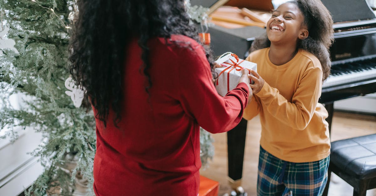 Can inheritance pass on to mother's dynasty? - Crop anonymous black woman passing gift box to cheerful daughter during New Year holiday at home Can inheritance pass on to mother's dynasty? - Crop anonymous black woman passing gift box to cheerful daughter during New Year holiday at home