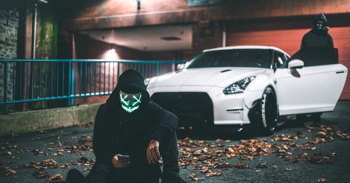 Can Xbox 360 and PS3 players go online together in Grand Theft Auto 5? [duplicate] - Anonymous male in neon mask browsing internet on cellphone while sitting on asphalt road covered with faded leaves near modern auto and friend standing on illuminated street at night