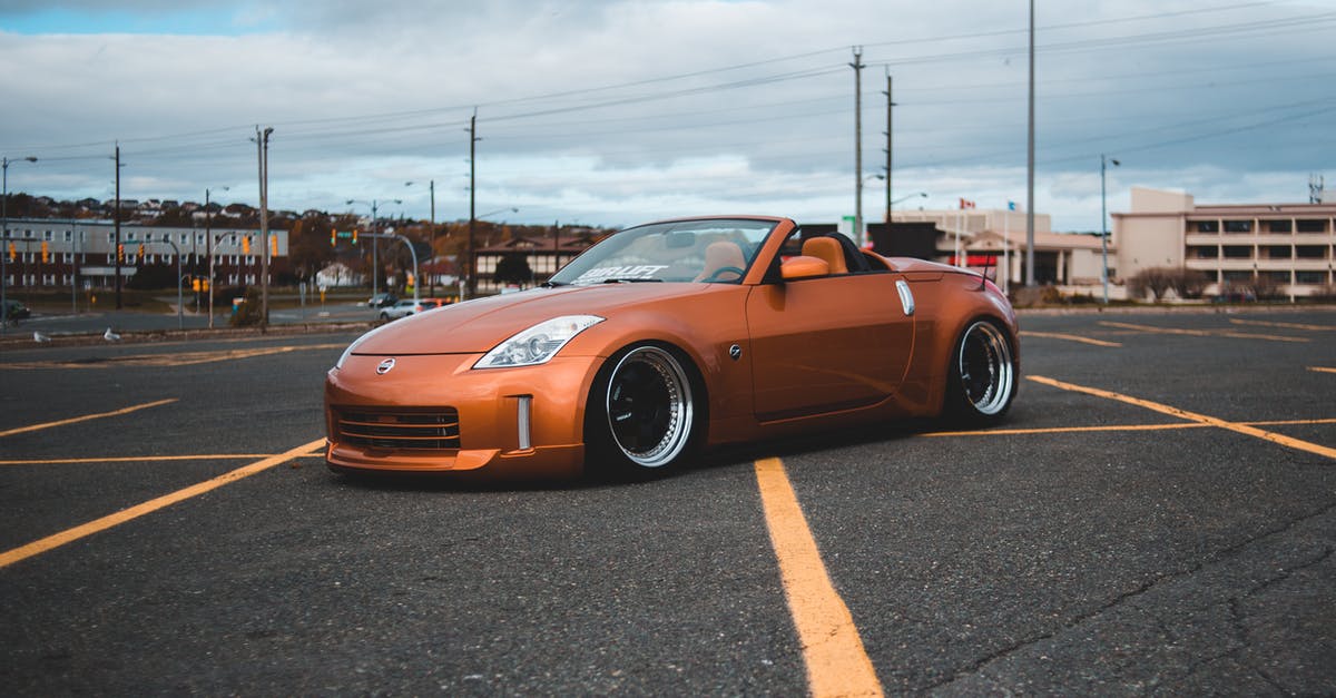 Can you build on top of every vehicle? - Side view of modern design orange automobile with convertible top on asphalt roadway with yellow marking lines behind buildings and lamp posts in town in daylight