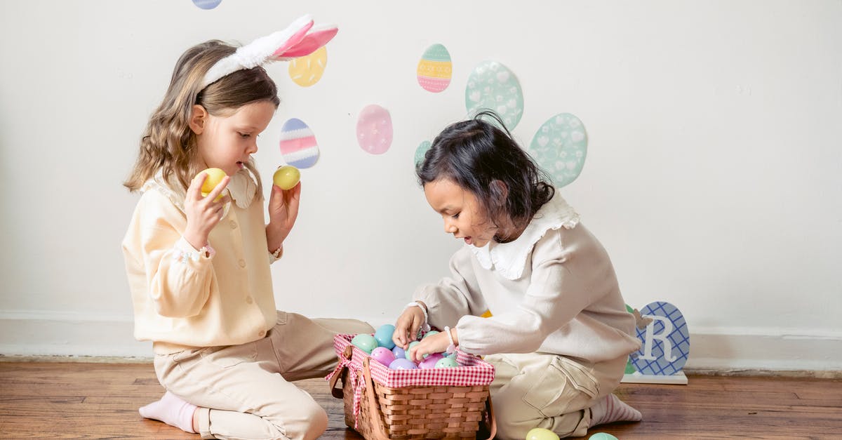 Can you choose which version of a game to play on Steam? - Side view of adorable little Hispanic girl choosing colorful Easter eggs while playing with friend on floor at home