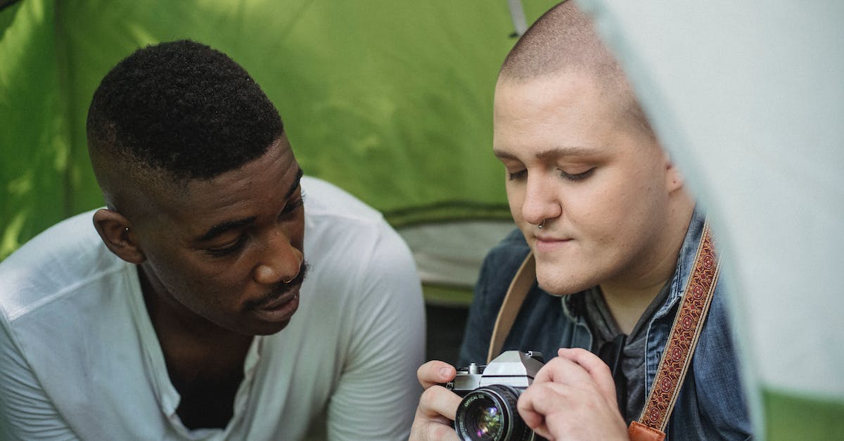 Can you convince old neighbours to move back in using the camping site? - Young male showing sharing retro photo camera with African American friend while sitting in green tent