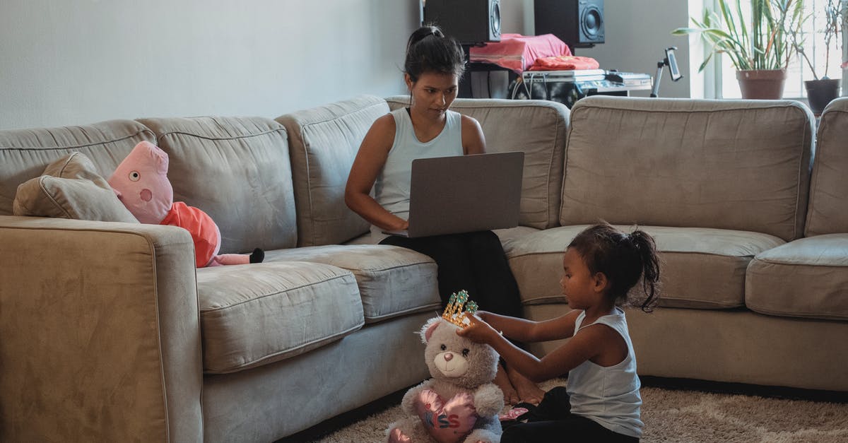 Can you play games between physical and online platforms (eg. Xbox Live & Xbox can play with PC & Steam)? - Mother working on computer while sitting on couch and daughter playing with toys on floor in living room